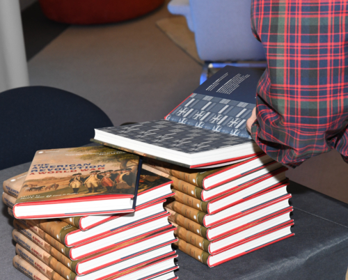 A person in plaid looking at the back cover of a Smithsonian exhibition books from the &quot;France and the American Revolution&quot; event April 21, 2019. © France in the US